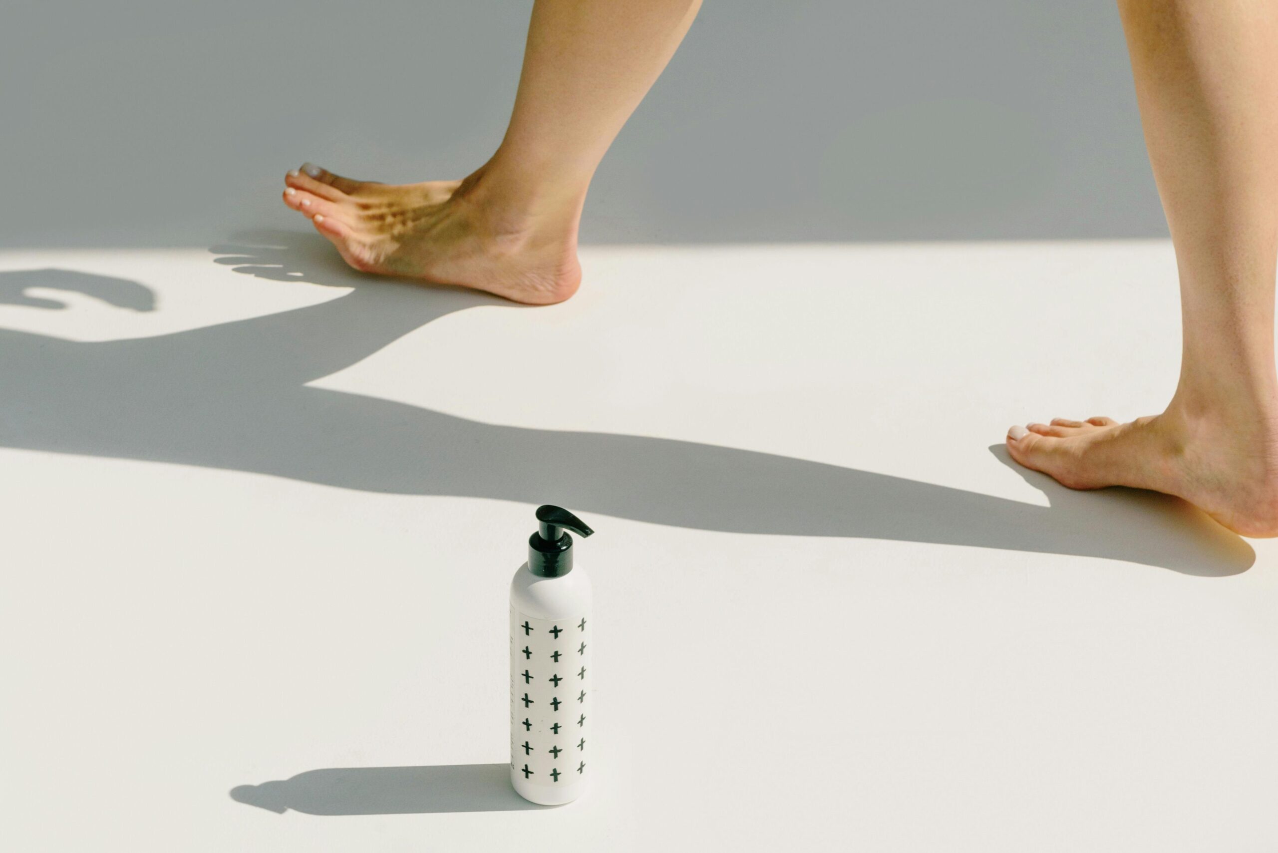 Close-up of bare feet and a pump bottle casting shadows in bright light.